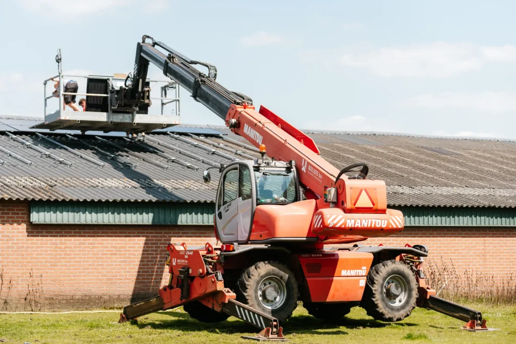 Verreiker met werkbak bij een stal waarop zonnepanelen worden gelegd