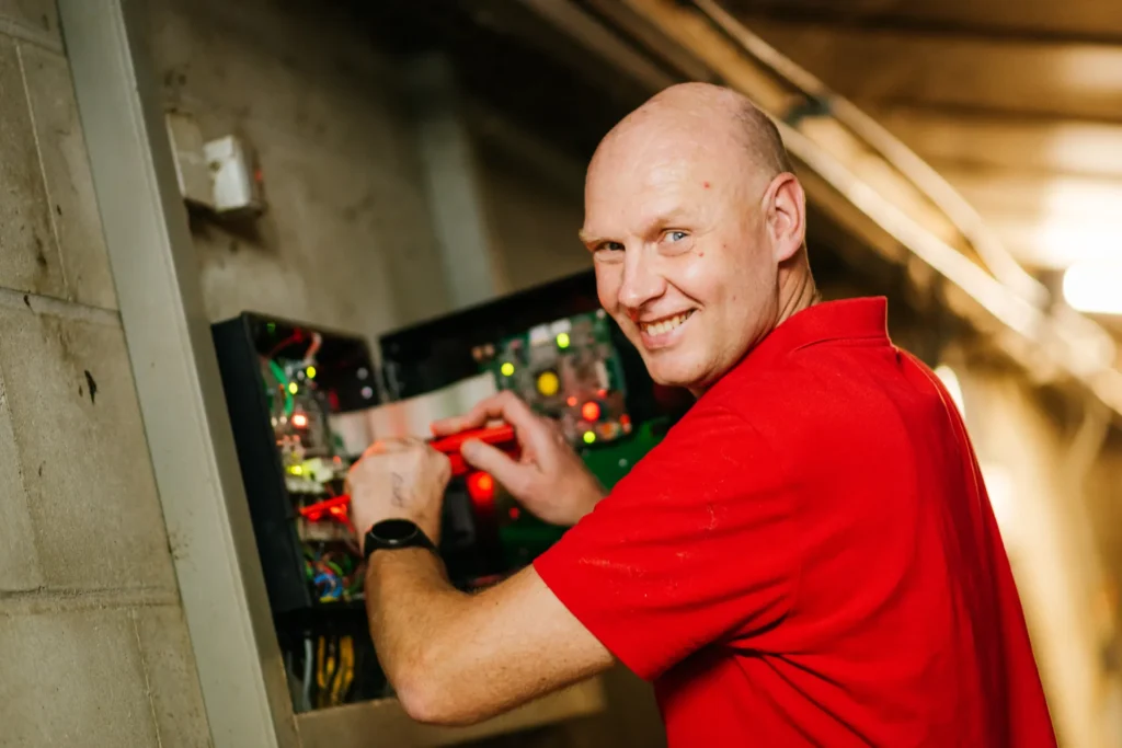 Monteur van Essink werkt lachend aan een besturingskast