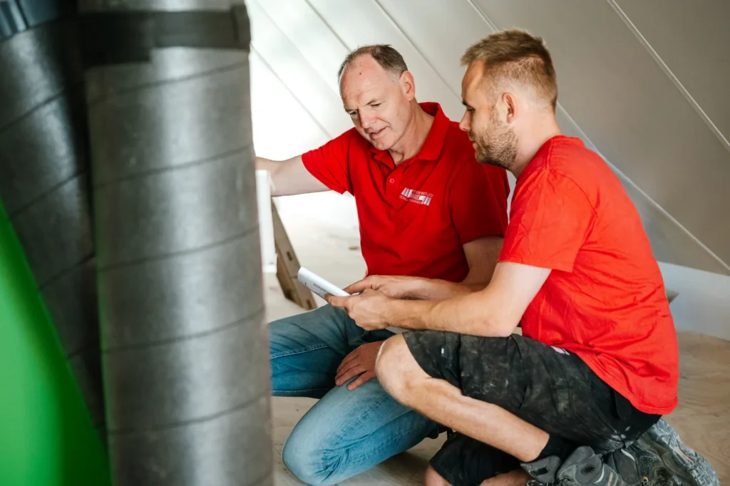 Twee monteurs overleggen op een zolder naast de ventilatie-unit